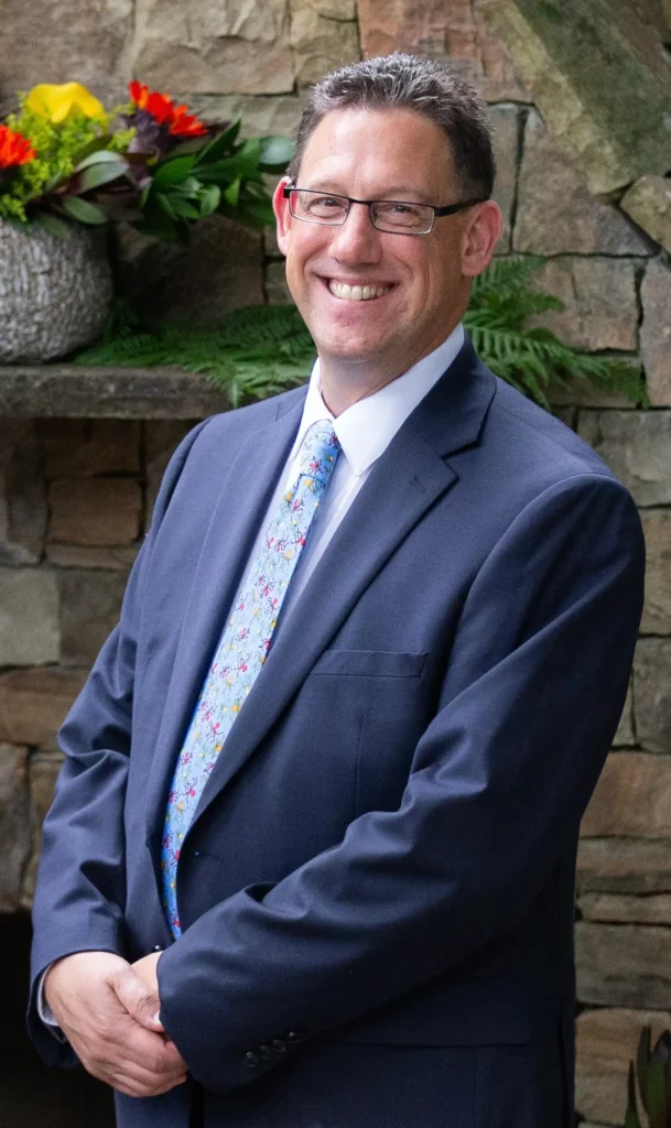 A man in a suit and tie standing with his hands crossed.